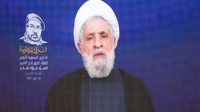 يظهر نعيم قاسم على شاشة، مرتدياً ملابس سوداء وعمامة بيضاء